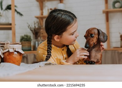 cute little girl at home in the kitchen bakes cookies with her pet dog dachshund. child with a pet in the kitchen - Powered by Shutterstock