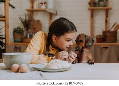 cute little girl at home in the kitchen bakes cookies with her pet dog dachshund. child with a pet in the kitchen - Powered by Shutterstock