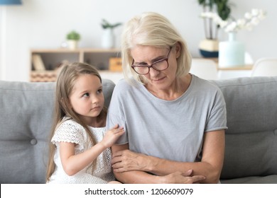 Cute Little Girl Hug Upset Grandmother Feel Sad And Down Comforting Her, Small Granddaughter Embrace Grandma Caressing Showing Empathy And Love, Grandchild Make Peace With Granny Asking Forgiveness