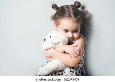 Cute little girl huggin toy puppy on grey background