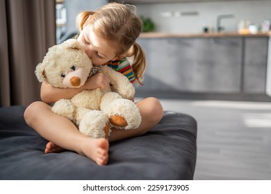 Cute little girl hugging teddy bear while sitting on sofa at home. High quality photo - Powered by Shutterstock