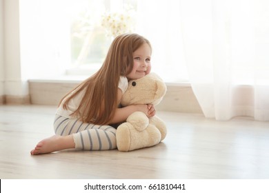 Cute little girl hugging teddy bear while sitting on floor at home - Powered by Shutterstock