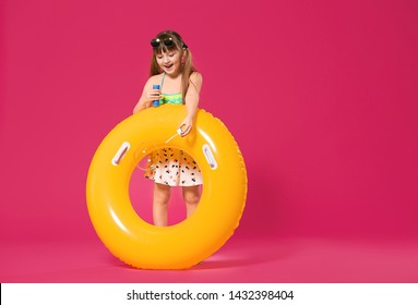 Cute little girl with inflatable ring blowing soap bubbles on color background