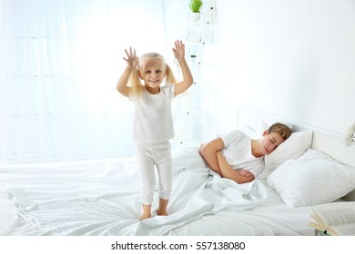 Cute little girl jumping on bed while her elder brother is sleeping