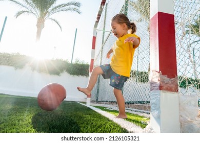 Cute little girl kicking soccer ball on green sports field at sunset time. Kid playing football with her family - Powered by Shutterstock