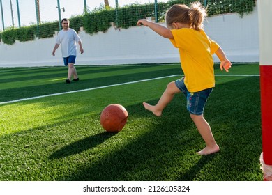 Cute little girl kicking soccer ball to father on green sports field at sunset time. Kid playing football with her family  - Powered by Shutterstock