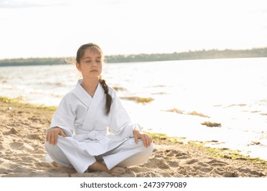 Cute little girl in kimono meditating near river. Karate practicing - Powered by Shutterstock