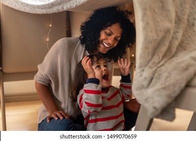 Cute Little Girl Laughing While Sitting In A Blanket Fort With Her Mother On Their Living Room Floor At Home