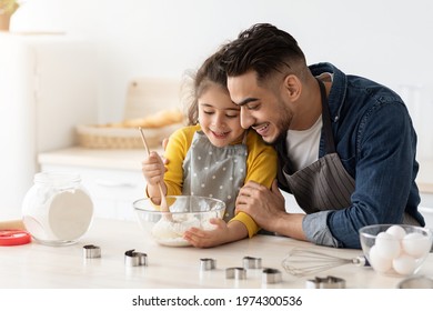 Cute Little Girl Learning How To Make Dough While Baking With Father In Kitchen, Caring Arab Dad Embracing Daughter While She Mixing Ingredients In Bowl, Enjoying Cooking Together, Closeup