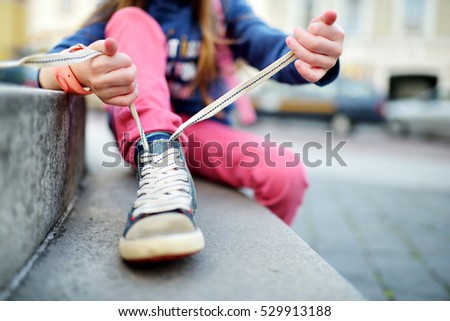 Cute little girl learning to tie shoelaces outdoors on summer day 