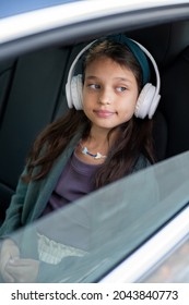 Cute Little Girl Listening To Music In Headphones While Sitting On Backseat Of Car And Looking Through Window