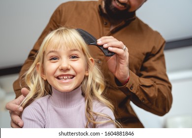 Cute Little Girl Looking At Camera And Smiling While Dad Brushing Her Hair Stock Photo