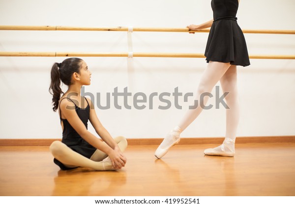Cute little girl looking\
up to her dance teacher while she performs a ballet routine next to\
a barre