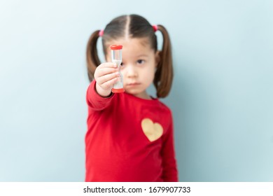 Cute Little Girl Looking At A Sand Timer With A Sad Face While She Is In Timeout. Focus On Timer