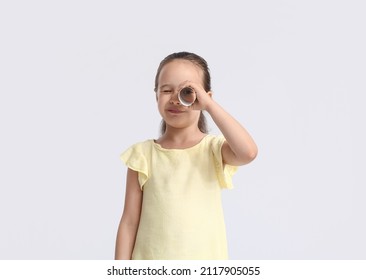 Cute little girl looking through tube of toilet paper on light background