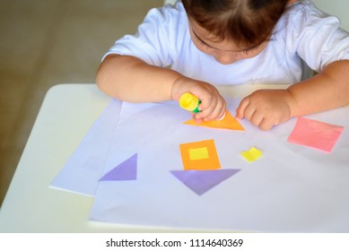 Cute little girl make applique, glues colorful house, applying a color paper using glue stick while doing arts and crafts in preschool or home. The idea for children's creativity, art project. 