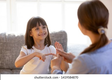 Cute little girl make hand gesture learning sign language with mom or female nanny, smiling small kid practice nonverbal talk with teacher at home, preschooler disabled child have lesson with tutor