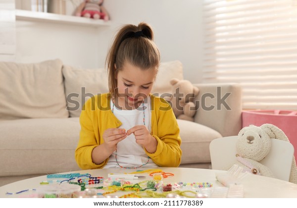 Cute
little girl making beaded jewelry at table in
room