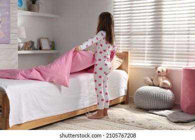 Cute little girl making bed at home