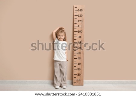 Cute little girl measuring height near beige wall