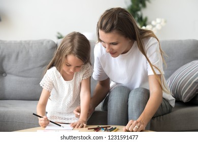 Cute little girl with mom or baby sitter drawing with colored pencils sitting on sofa, nanny or mother teaching preschool kid daughter playing together, educational hobbies for creative child concept