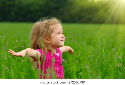 Cute Little Girl On The Meadow In Spring Day. Child Running On Field . Child With Arms Outstretched. Freedom Concept.