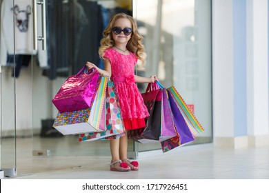 Cute Little Girl On Shopping. Portrait Of A Kid With Shopping Bags. Child In Dress, Sunglasses And Shoes Near Shopping Mall Having Fun. Shopping. Girl. 