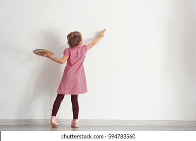 Cute little girl painting wall in empty room