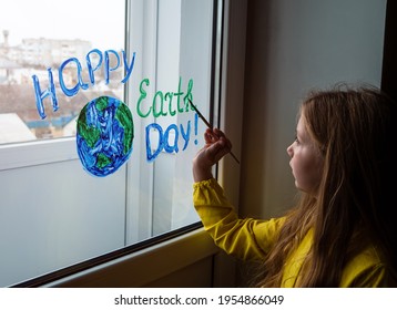 Cute Little Girl Painting Planet On Window At Home. Happy Earth Day April 22 Greeting Message. Creative Family Leisure Lockdown New Reality. Ecology Saving Environment Conscious Consumption Concept.