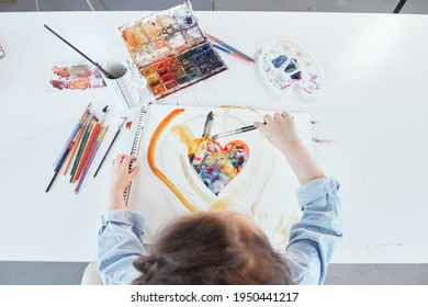 Cute Little Girl Painting Using Watercolor Paints. Top View Of Charming Little Girl Painting Heart Using Watercolors At The Table In Her Room At Home With Notebook Nearby. High Quality Photo