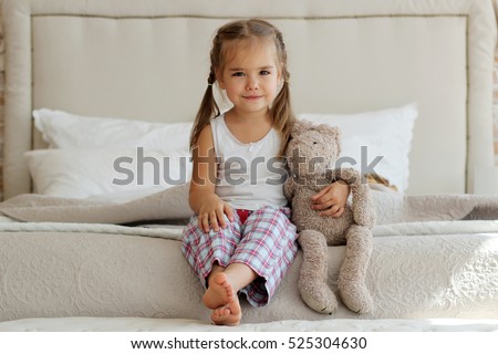 Cute little girl in pajama hugging her toy hare on the bed at home, happy childhood concept, indoor horizontal portrait