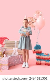 Cute little girl in party hat with Birthday gifts on pink background