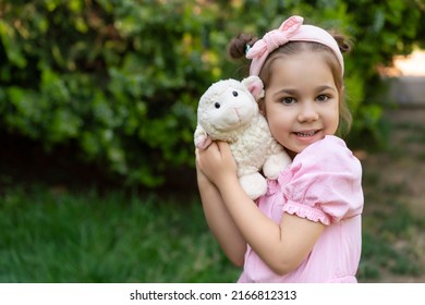 Cute little girl in pink dress with toy sheep. Portrait of happy child celebrate sacrificial feast (aka: Eid-al-Adha). Festival of sacrifices and kid. Preschooler outdoor.