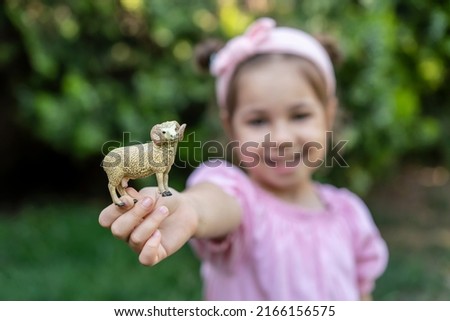 Cute little girl in pink dress with toy sheep. Portrait of happy child celebrate sacrificial feast (aka: Eid-al-Adha). Festival of sacrifices and kid. Preschooler outdoor.