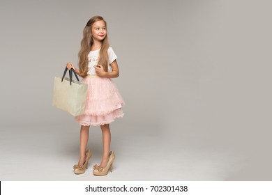 Cute Little Girl In Pink Tulle Skirt And Too Big Shoes Holding Packages In Hand