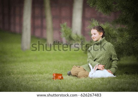 Cute little girl play with white easter bunny rabbit at green grass background. Concept of spring celebration, pet care, child and animal friendship, nature and wildlife learn classes, hare adoption