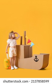 Cute Little Girl Playing With Cardboard Ship On Yellow Background