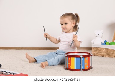 Cute little girl playing with drum and drumsticks at home - Powered by Shutterstock