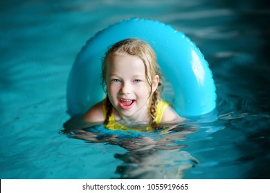 Cute Little Girl Playing With Inflatable Ring In Indoor Pool. Child Learning To Swim. Kid Having Fun With Water Toys. Family Fun In A Pool.