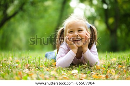 Cute little girl is playing with leaves in autumn park