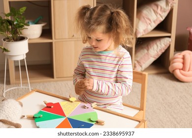 Cute little girl playing matching game with clothespins at home