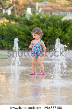 Cute little girl playing on a urban jet fountains with water splashing around. Selective focus with blurred background. concept of summer and happy childhood