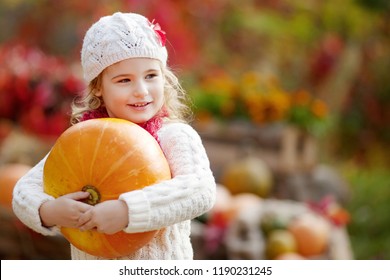 Cute little girl playing with pumpkins in autumn park. Autumn activities for children. Halloween and Thanksgiving time fun for family.