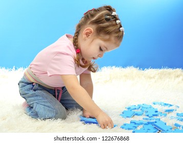 cute little girl playing with puzzles, on blue background