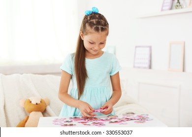 Cute little girl playing with puzzles on home interior background