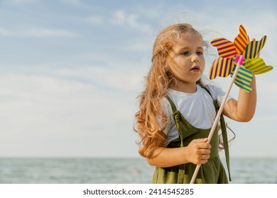 Cute little girl playing with windmill on the sunny beach. Active caucasian small daughter kid child spending time outdoors along river lake sea - Powered by Shutterstock