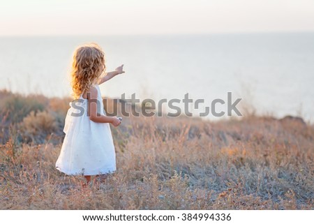 Cute little girl pointing with finger on sea