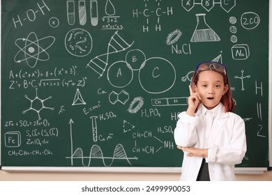 Cute little girl pointing up near chalkboard at chemistry lesson in classroom - Powered by Shutterstock