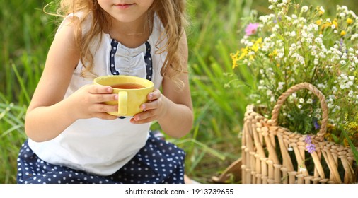 Cute Little Girl Portrait, Caucasian With Curls Sitting On A Picnic In The Summer And Holding In Hand A Large Yellow Cup With Herbal Tea. Tea Ceremony. Childhood.Summer Concept. Copy Space On The Righ