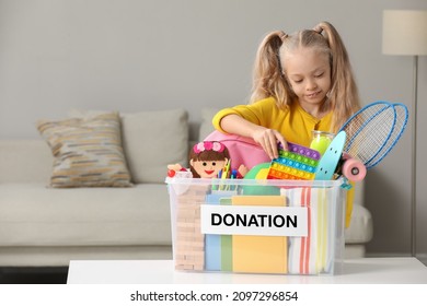 Cute little girl putting toy into donation box at home, space for text